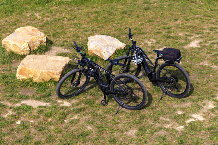 Two electric bicycles stand in a meadow near the stones. Top view. Bicycle helmets hang on the handlebars Two electric bicycles stand in a meadow near the stones.