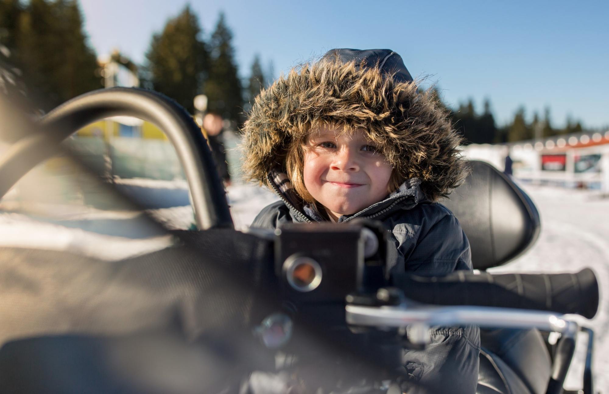 iStock-615835204-min Cute boy enjoying while sitting on a snowmobile at ski resort and looking at the camera.