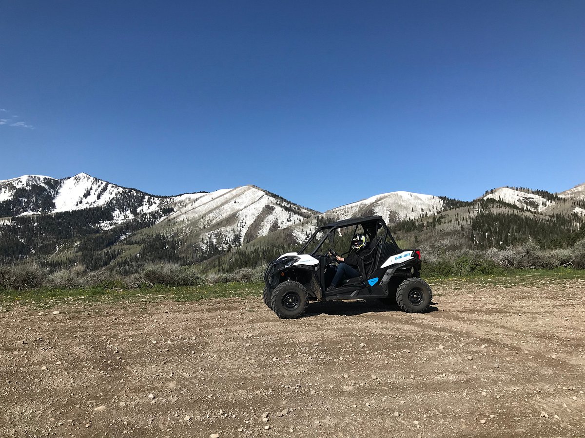 uinta-recreation-15 Person driving an off-road vehicle against a backdrop of snow-capped mountains under a clear blue sky.