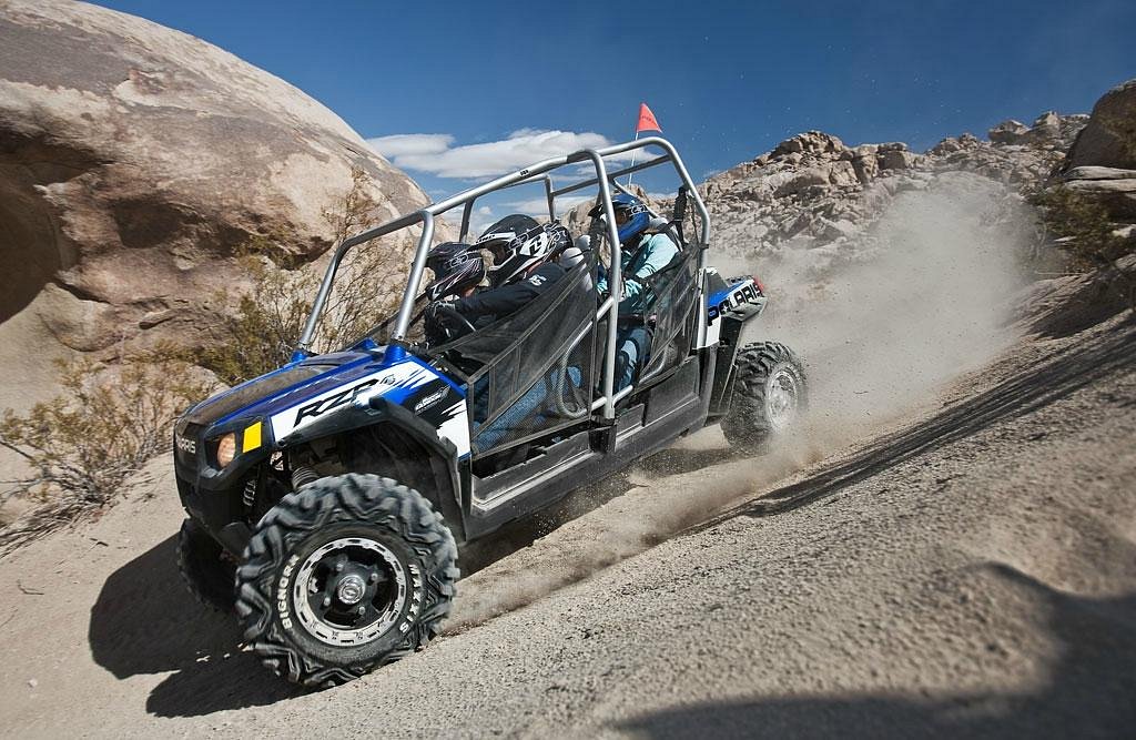 ATV driving uphill on a rocky desert terrain under clear blue sky.