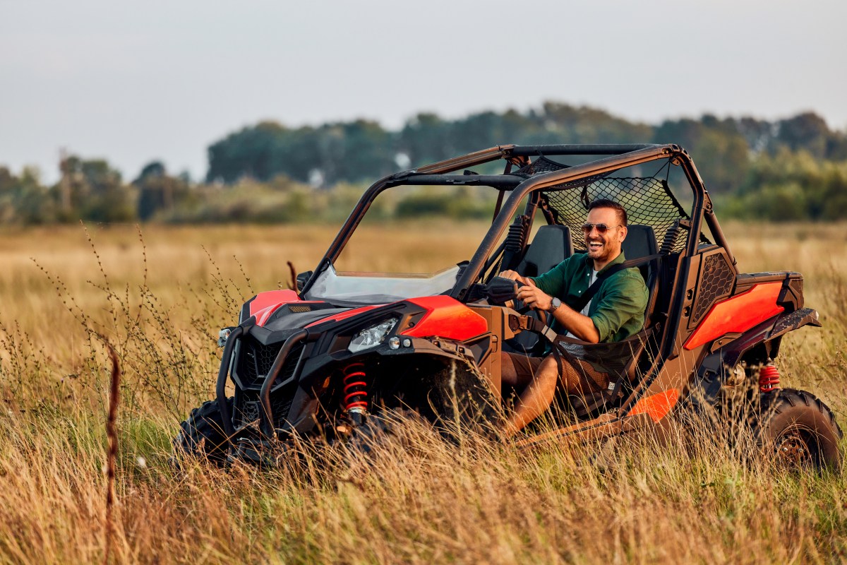 A smiling man with sunglasses enjoying a Can-Am Commander XT while off-roading in Utah.