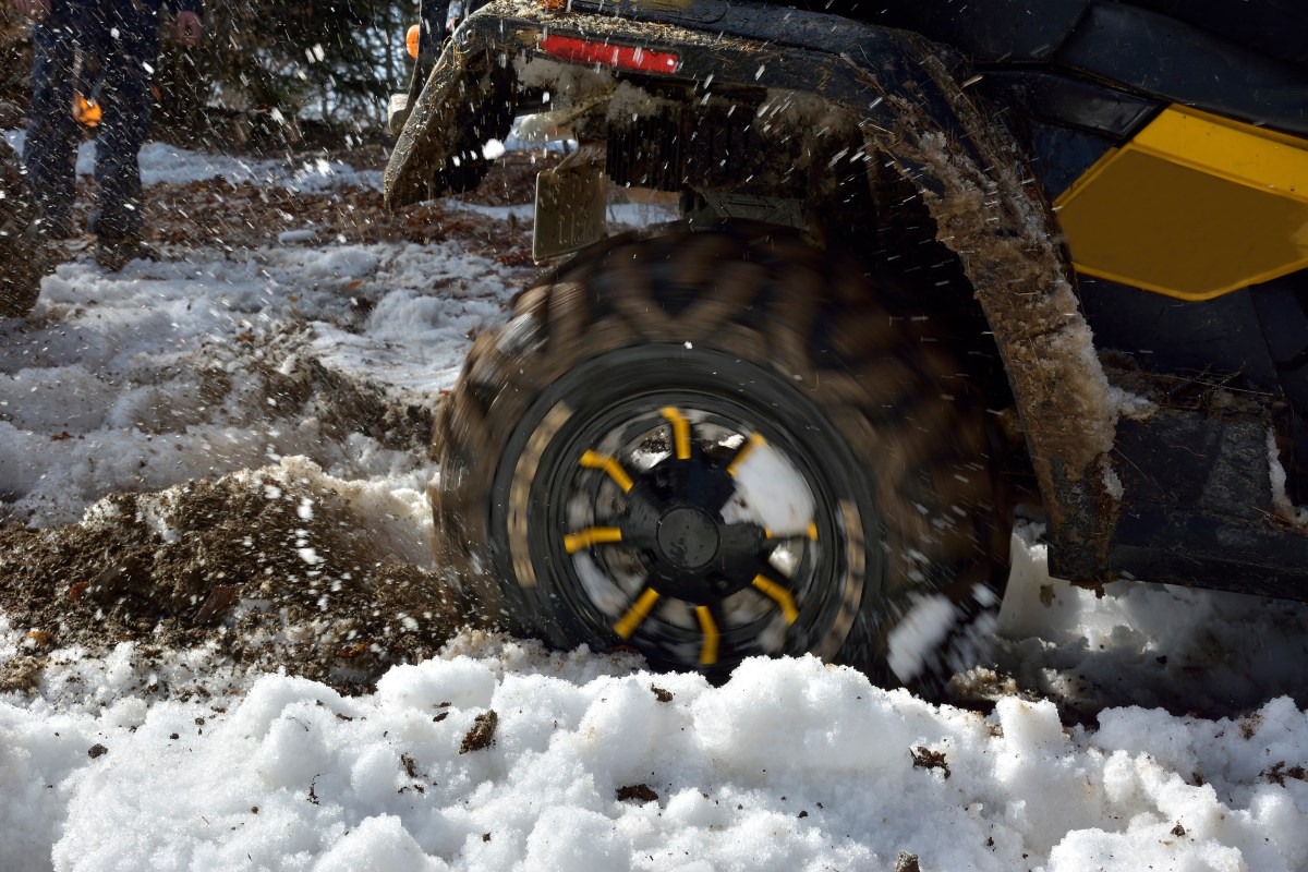 A Defender Max HD11 quad bike in the winter field with the wheel spinning up dirt and snow.