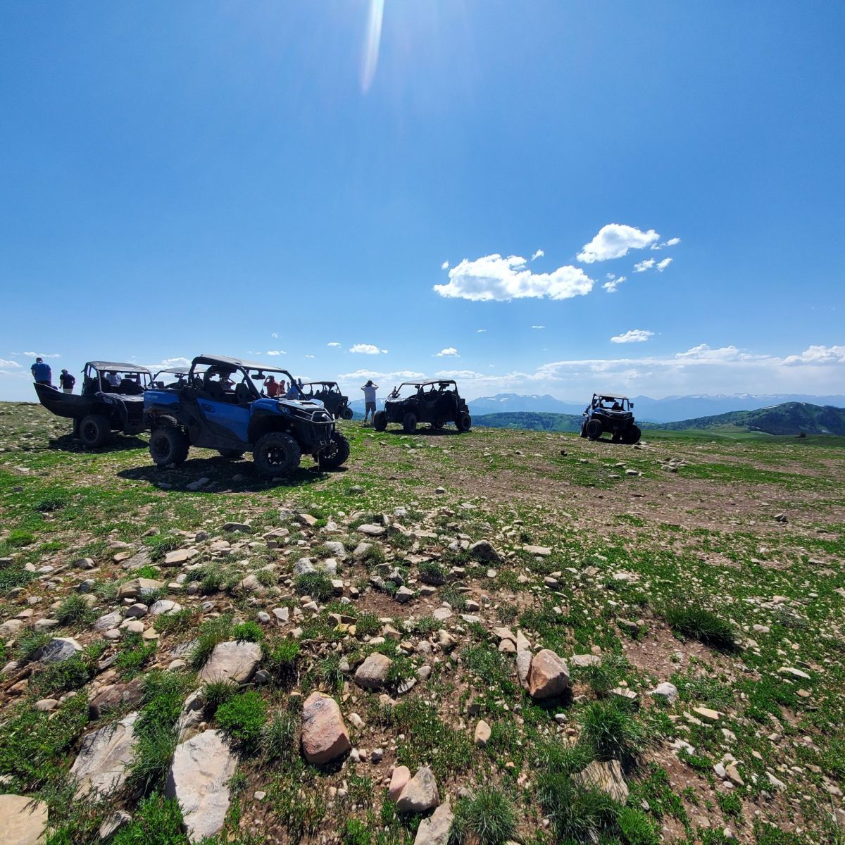 A group of Can-Am off-road UTVs parked at a viewpoint in Utah, grouped with people walking around, talking, and taking photos.