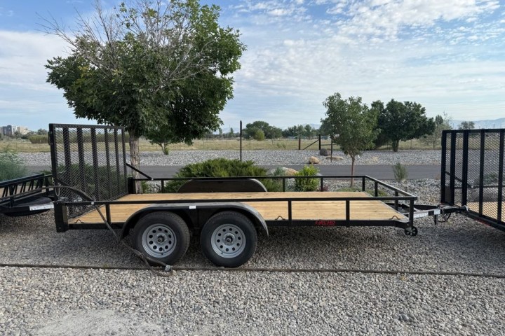 Open flatbed trailer on gravel, trees and cloudy sky in background.