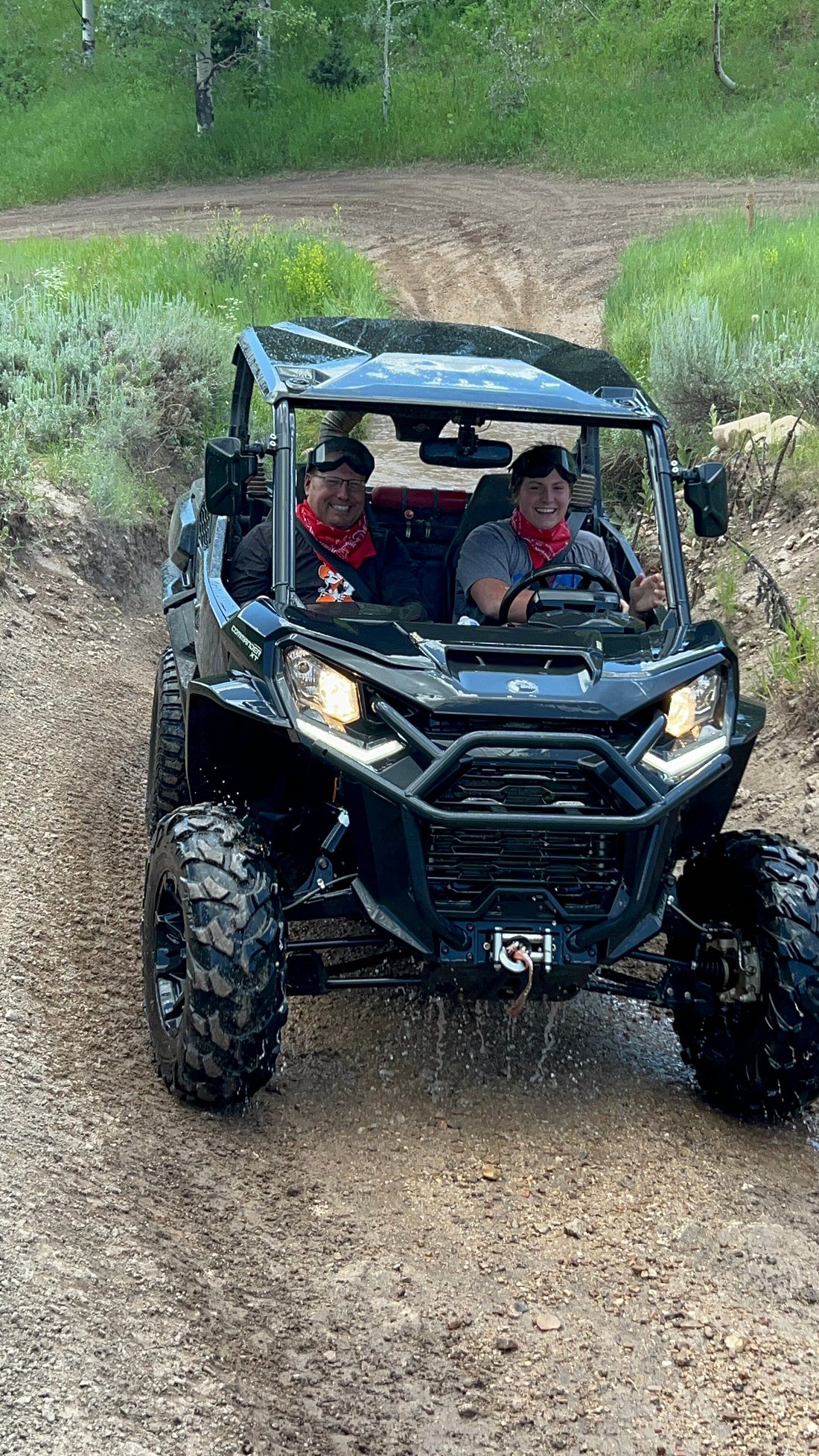 A man and woman riding through a large puddle in a Can-Am UTV on the trail through Cascade Springs in Utah.