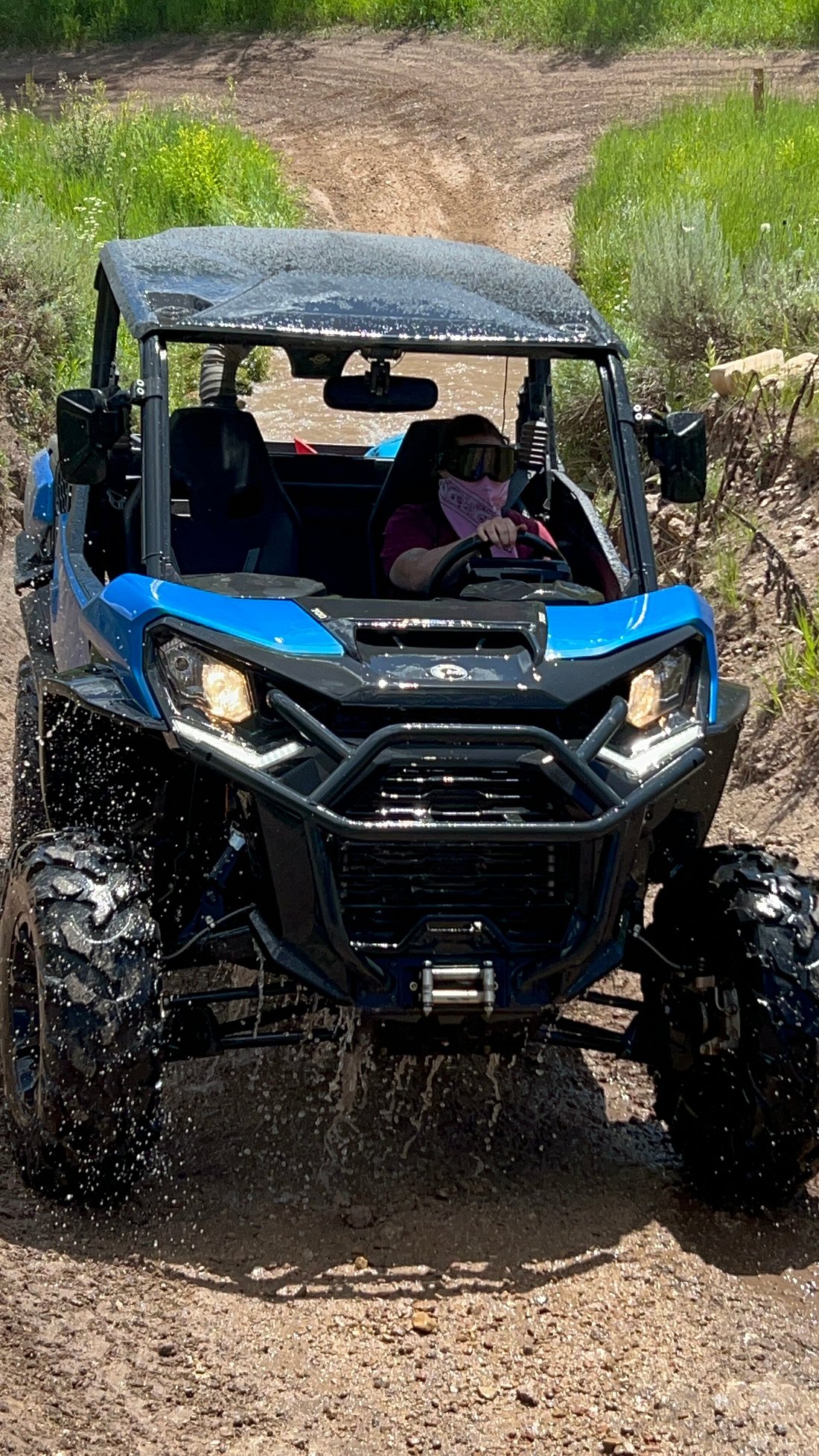 A woman with a face covering riding through a puddle in a Can-Am UTV on the Cascade Springs trail in Utah.