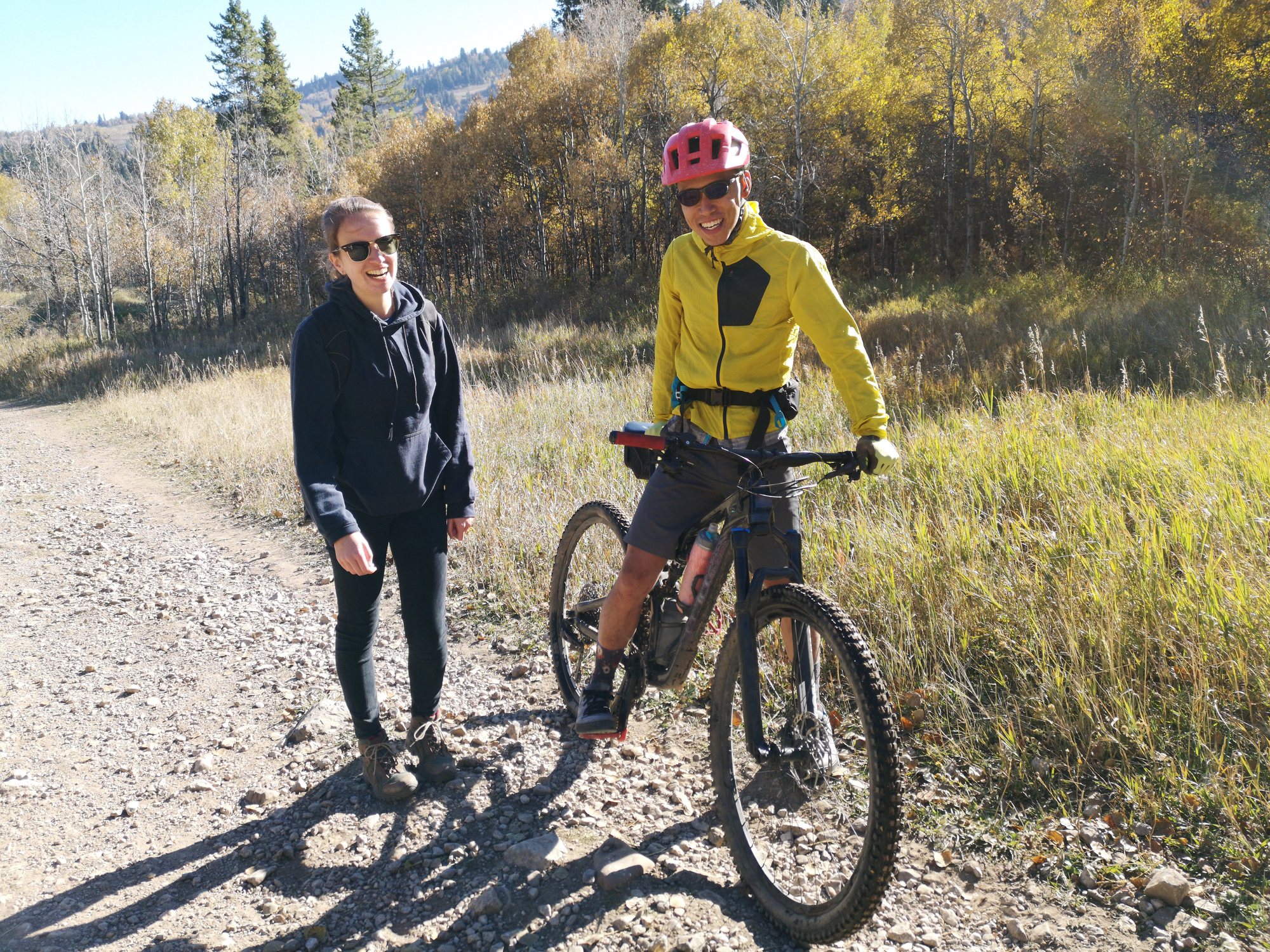 A man on an electric bike rental and a woman hiking who are both smiling at the camera on a trail near Park City, UT.