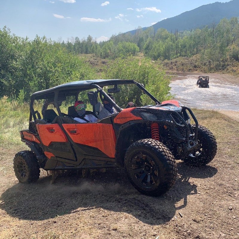 Side view of a Can-Am side-by-side vehicle in Utah with another UTV in the background driving through a large puddle of water on the trail.