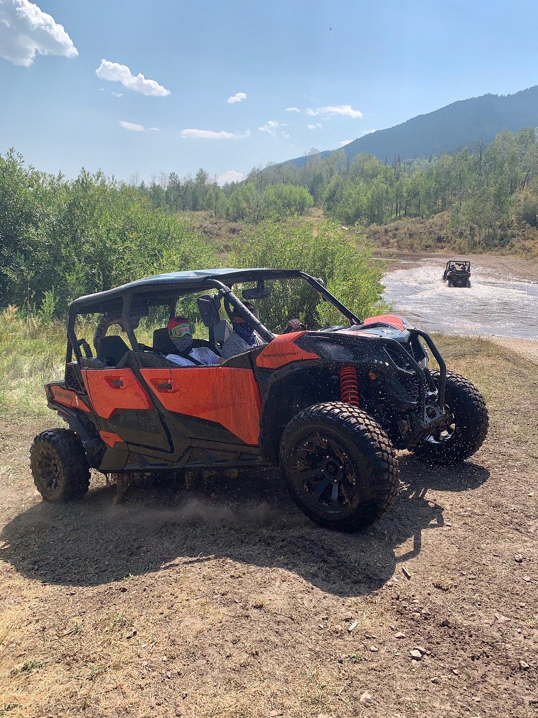 Side view of a Can-Am side-by-side vehicle in Utah with another UTV in the background driving through a large puddle of water on the trail.