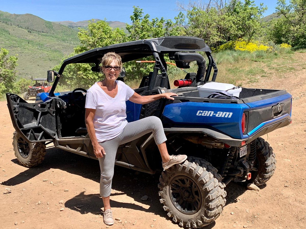A woman standing in front of a Can-Am with her foot on the wheel on a trail during a guided UTV tour in Heber City, Utah.
