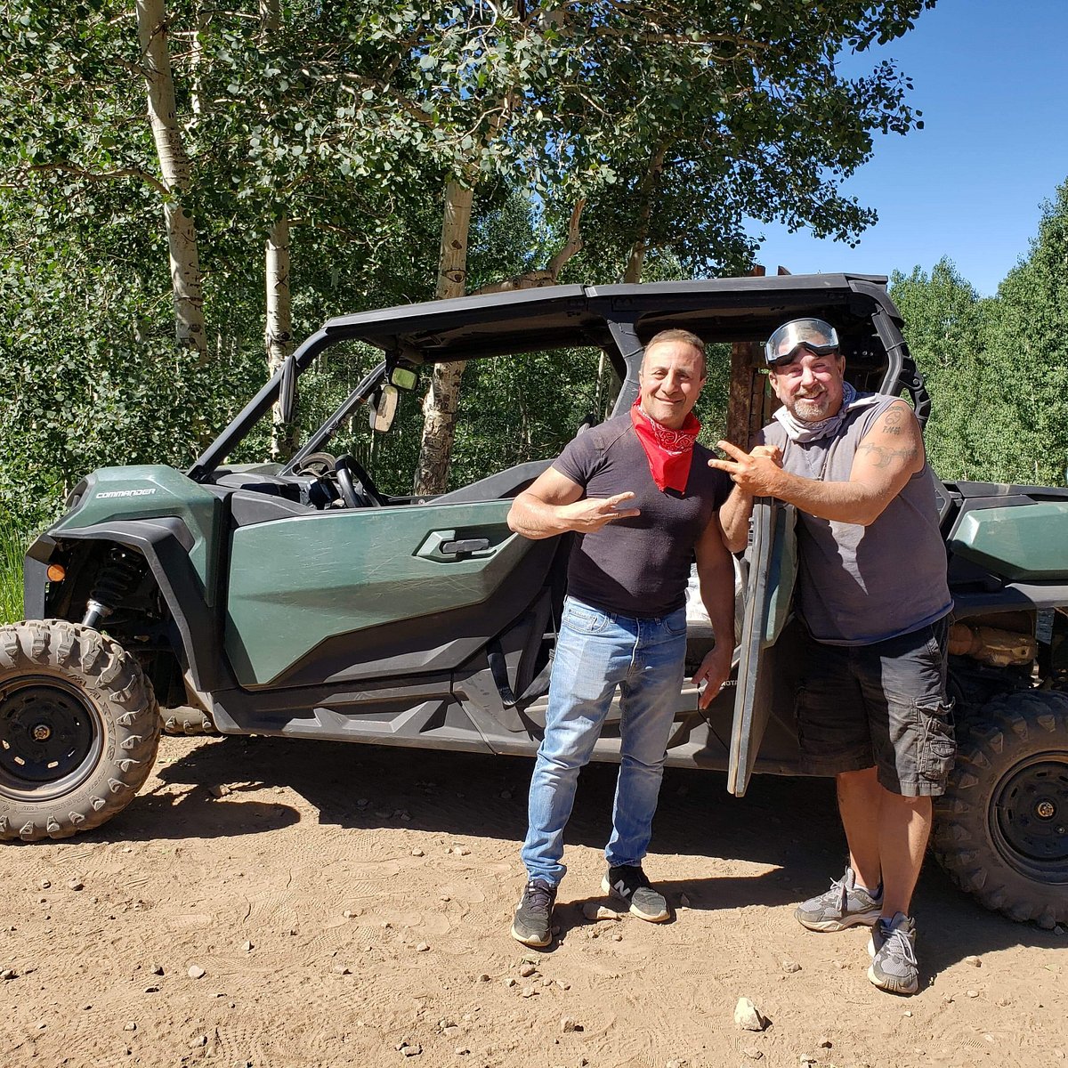 Two guys throwing up the peace sign while standing in front of a Can-Am on a trail during a guided UTV tour in Heber City, Utah.
