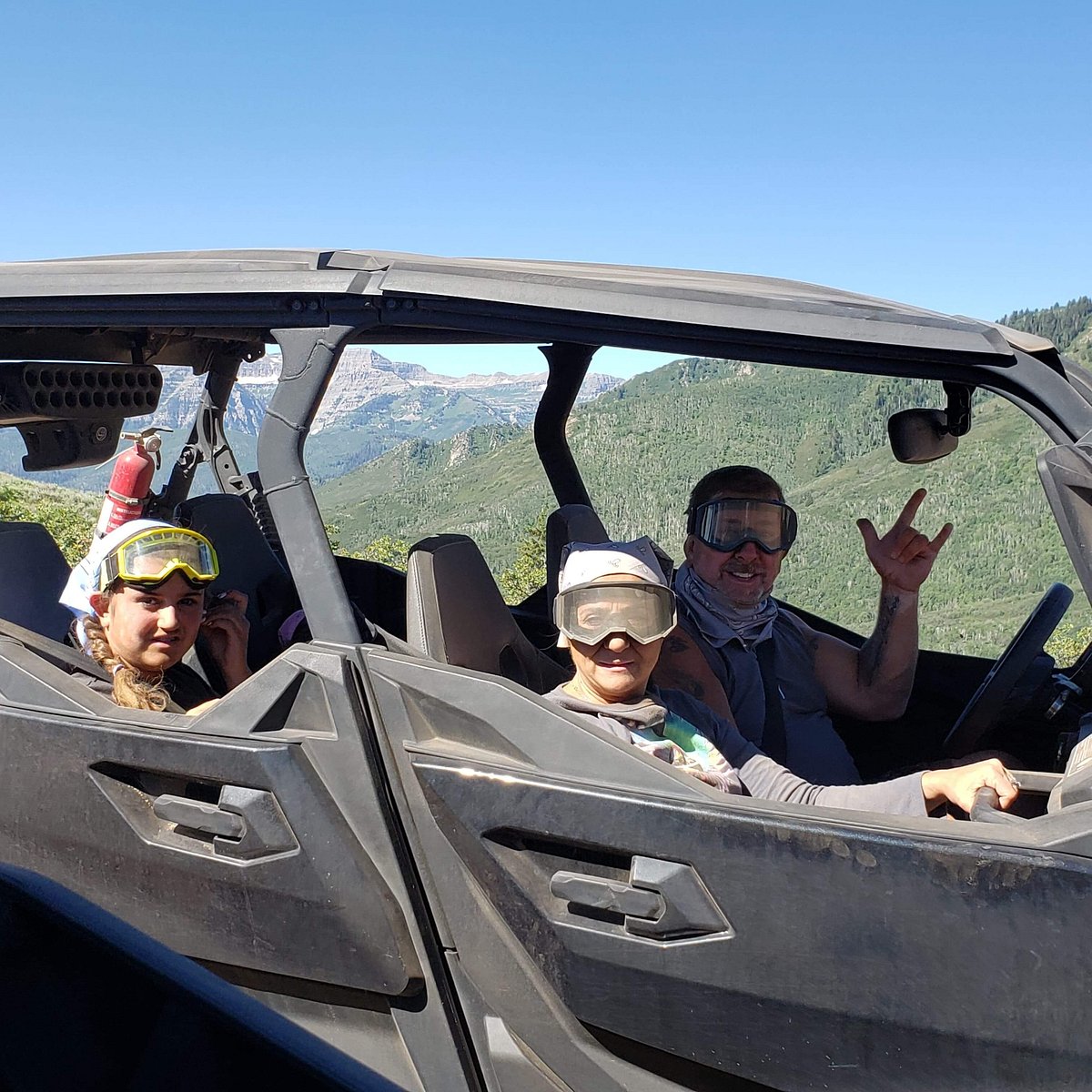 A close-up of a family smiling and throwing up the love sign inside of a Can-Am UTV in Utah.