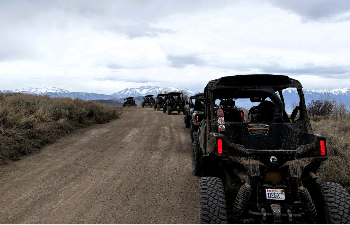 ATVs driving on a dirt road with mountains in the background.
